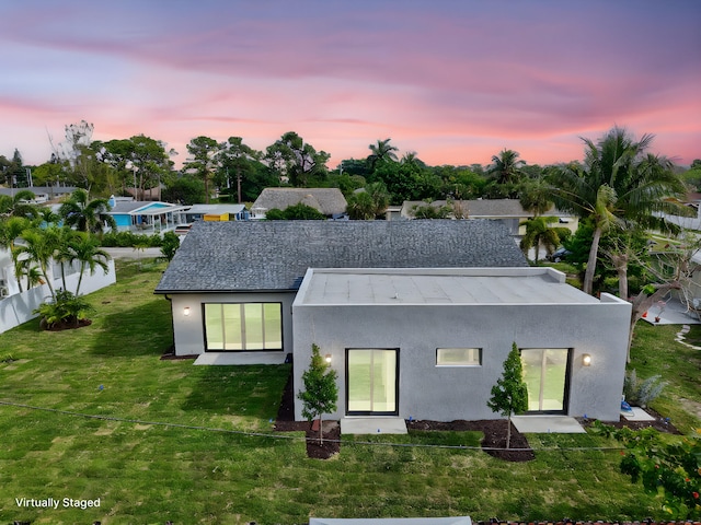 back of house at dusk featuring fence, a lawn, and stucco siding