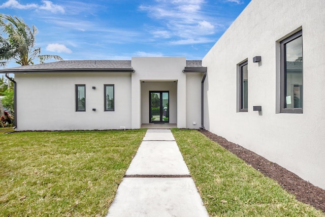 view of exterior entry featuring a yard, stucco siding, and french doors