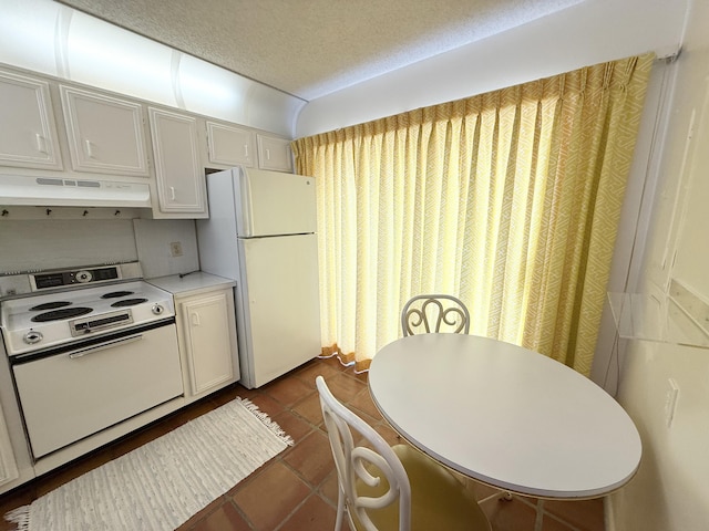 kitchen featuring light countertops, a textured ceiling, under cabinet range hood, white appliances, and dark tile patterned flooring