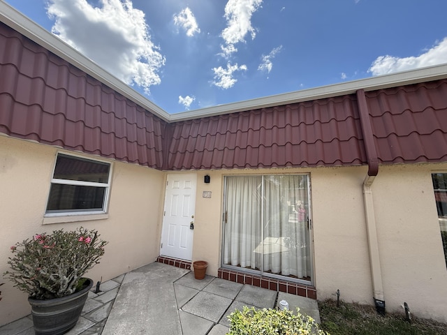entrance to property featuring stucco siding, mansard roof, a tiled roof, and a patio