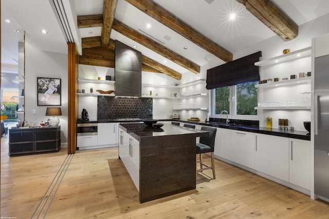 kitchen featuring open shelves, island range hood, a sink, lofted ceiling with beams, and tasteful backsplash