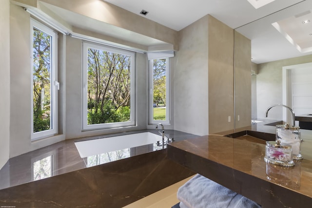 bathroom featuring a garden tub, a sink, and a healthy amount of sunlight