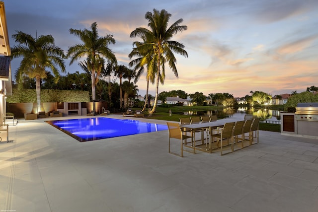 pool featuring a water view, outdoor dining area, a patio, exterior kitchen, and area for grilling