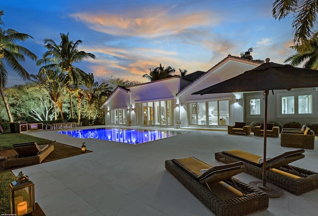 pool at dusk featuring an outdoor pool, french doors, and a patio