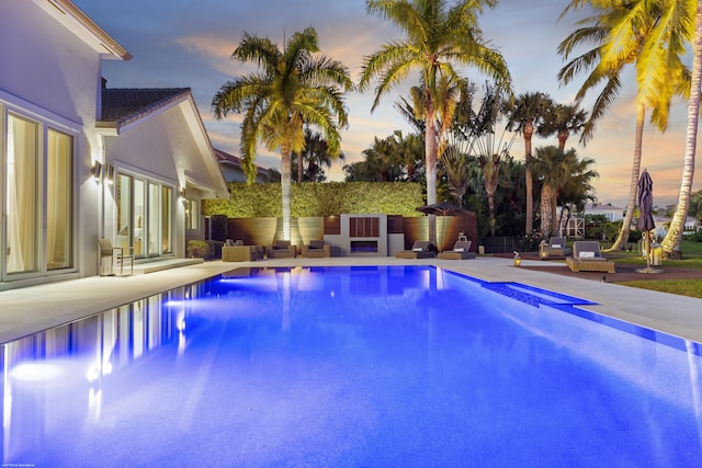 pool at dusk featuring outdoor lounge area, a patio area, and a fenced in pool