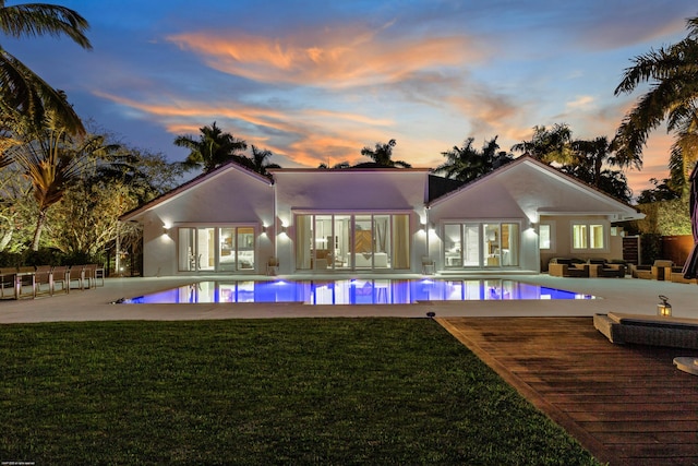 back of house at dusk with stucco siding, an outdoor pool, and a yard