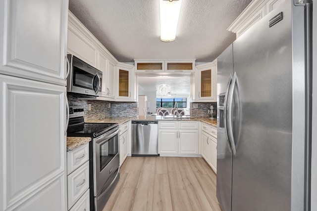 kitchen featuring decorative backsplash, glass insert cabinets, light wood-style floors, a textured ceiling, and appliances with stainless steel finishes