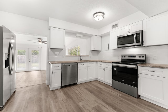 1134 NW 18th Ave, Fort Lauderdale, FL 33311 - kitchen featuring decorative backsplash, white cabinets, light wood finished floors, appliances with stainless steel finishes, and a sink