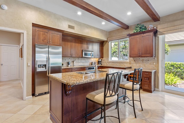 kitchen with an island with sink, backsplash, visible vents, light tile patterned floors, and appliances with stainless steel finishes