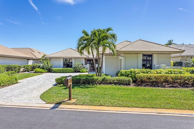 ranch-style house featuring stucco siding, a tile roof, decorative driveway, and a front lawn