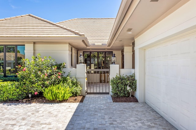 view of exterior entry with a gate, an attached garage, a tiled roof, and stucco siding