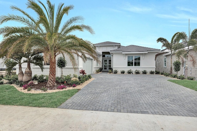 view of front of home with an attached garage, decorative driveway, stucco siding, and french doors