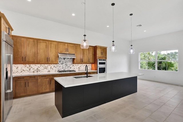 kitchen featuring appliances with stainless steel finishes, a sink, brown cabinetry, decorative backsplash, and under cabinet range hood