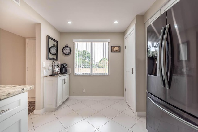 kitchen featuring baseboards, white cabinetry, fridge with ice dispenser, and light stone counters
