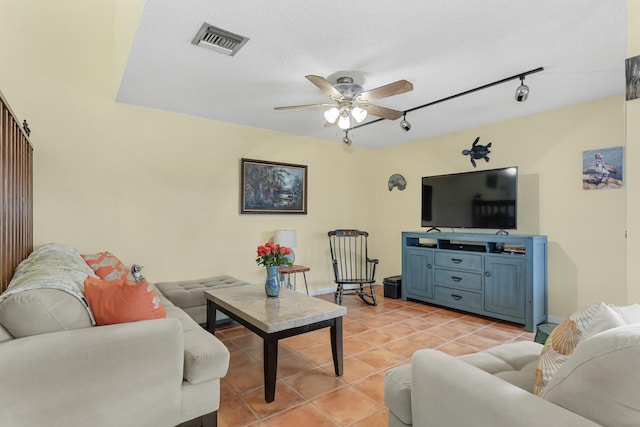 living room with a textured ceiling, visible vents, rail lighting, ceiling fan, and light tile patterned floors