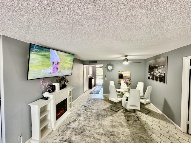 dining room featuring visible vents, a textured ceiling, a warm lit fireplace, and ceiling fan
