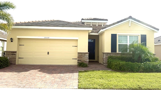 view of front of house featuring decorative driveway, stucco siding, stone siding, and a garage