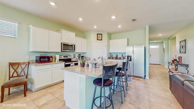 10577 SW Toren Way, Port Saint Lucie, FL 34987 - kitchen featuring appliances with stainless steel finishes, white cabinets, light tile patterned floors, a kitchen breakfast bar, and an island with sink