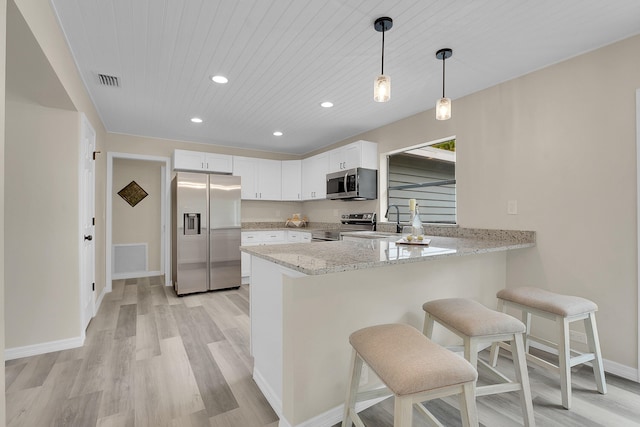 1701 SE Floresta Dr, Port Saint Lucie, FL 34983 - kitchen featuring appliances with stainless steel finishes, a peninsula, a breakfast bar area, white cabinetry, and light stone countertops