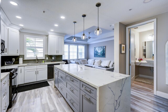 kitchen featuring black appliances, a sink, a center island, open floor plan, and light wood-style floors
