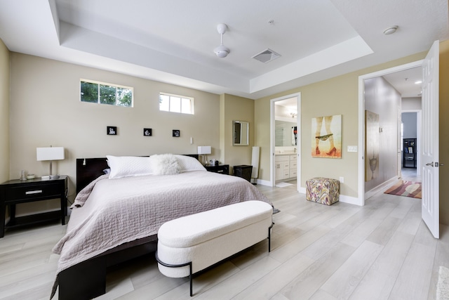 bedroom with a tray ceiling, light wood finished floors, baseboards, and ensuite bathroom