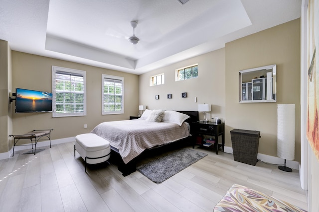 bedroom with a tray ceiling, wood finished floors, and baseboards