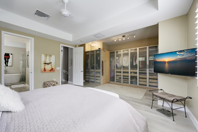 bedroom with wood finished floors, a raised ceiling, baseboards, and connected bathroom