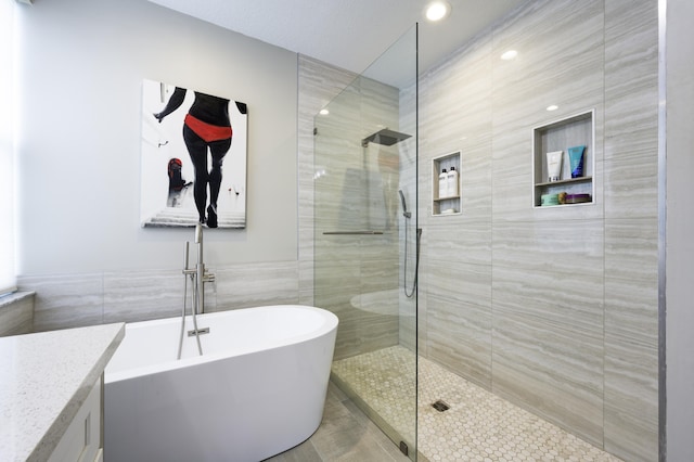 full bathroom featuring tile walls, a freestanding bath, a walk in shower, vanity, and recessed lighting