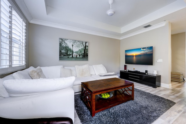 living area with light wood-style flooring, a raised ceiling, plenty of natural light, and ornamental molding