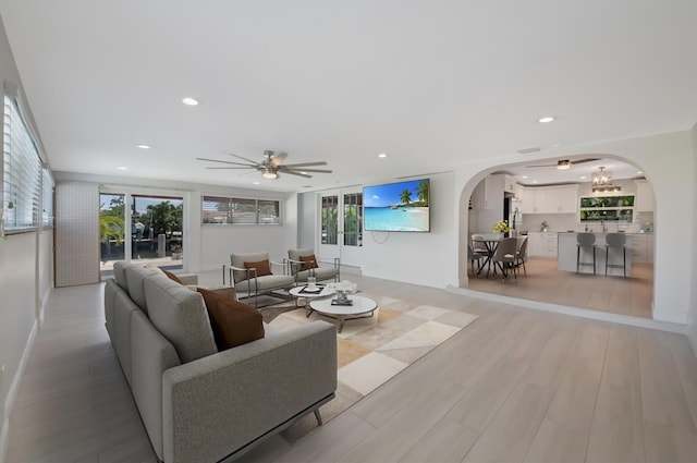 living room with arched walkways, ceiling fan, recessed lighting, and light wood-style floors