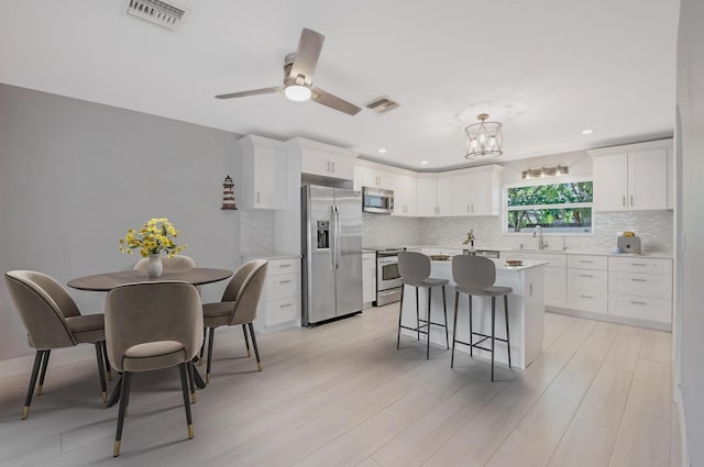 kitchen featuring stainless steel appliances, a breakfast bar, tasteful backsplash, white cabinetry, and recessed lighting