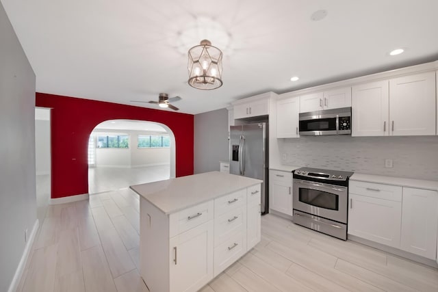 kitchen featuring appliances with stainless steel finishes, arched walkways, decorative backsplash, light countertops, and white cabinets