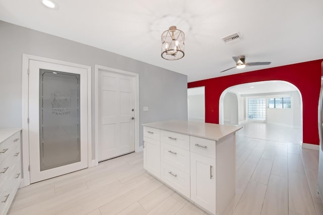 kitchen featuring arched walkways, white cabinets, light countertops, and a ceiling fan