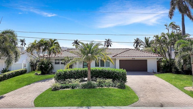 mediterranean / spanish house featuring decorative driveway, stucco siding, an attached garage, a tiled roof, and a front lawn