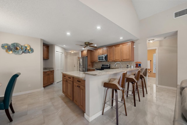 kitchen featuring light stone countertops, a kitchen breakfast bar, a peninsula, stainless steel appliances, and visible vents