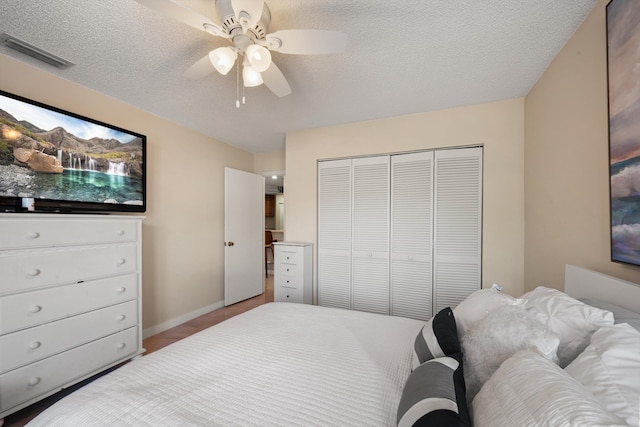 bedroom with a closet, a textured ceiling, visible vents, baseboards, and ceiling fan