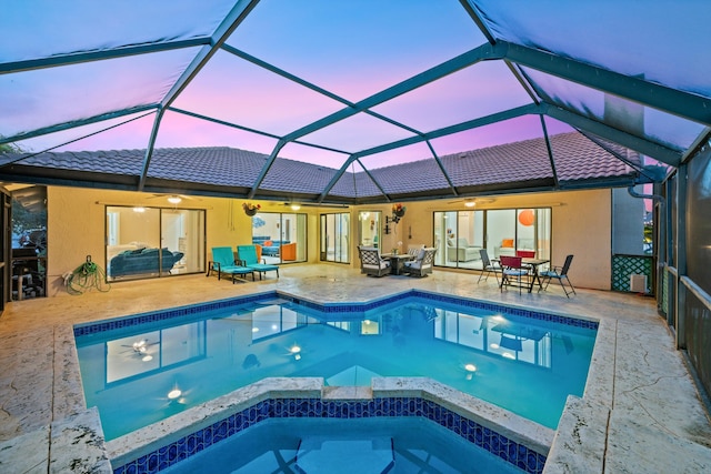 pool at dusk featuring a lanai, a patio, outdoor dining space, ceiling fan, and a pool with connected hot tub