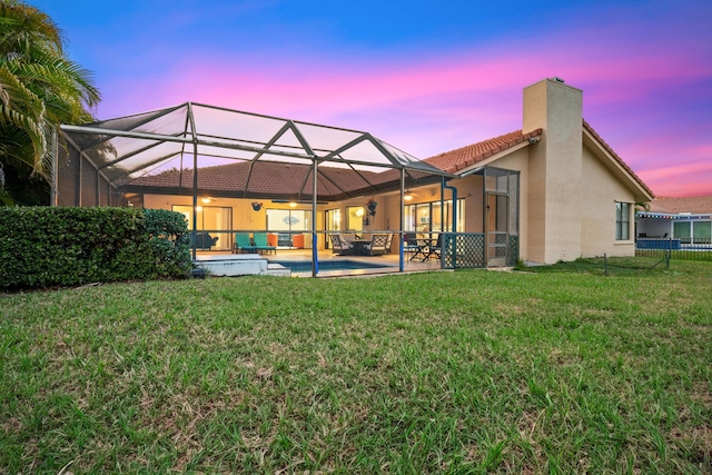 back of property at dusk featuring a lanai, a patio, a chimney, a tile roof, and a yard