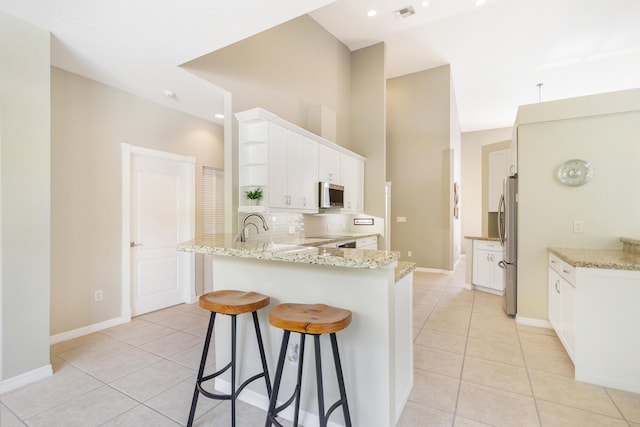 kitchen with light tile patterned flooring, a peninsula, a breakfast bar, stainless steel appliances, and tasteful backsplash