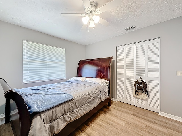 bedroom featuring a closet, wood finished floors, a textured ceiling, baseboards, and visible vents