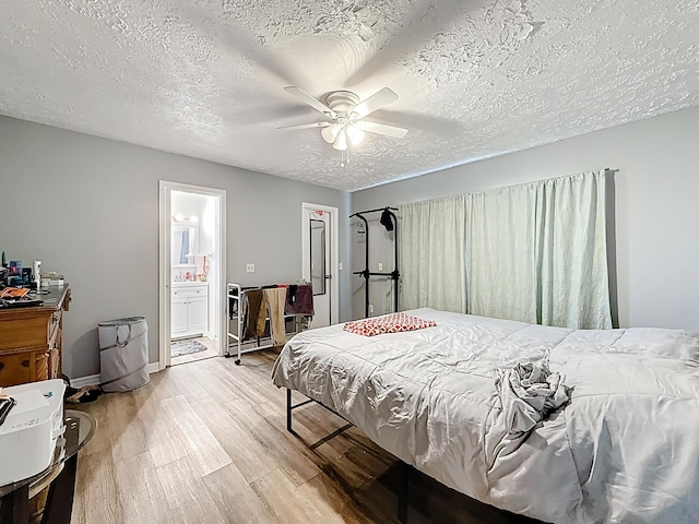 bedroom with light wood-type flooring, baseboards, a textured ceiling, ensuite bath, and a ceiling fan