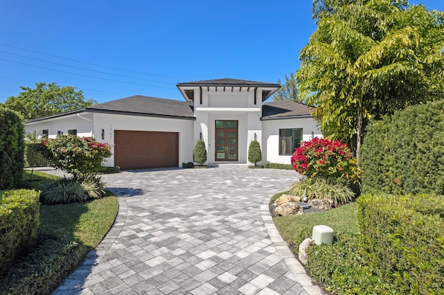prairie-style house with decorative driveway, an attached garage, roof with shingles, stucco siding, and french doors