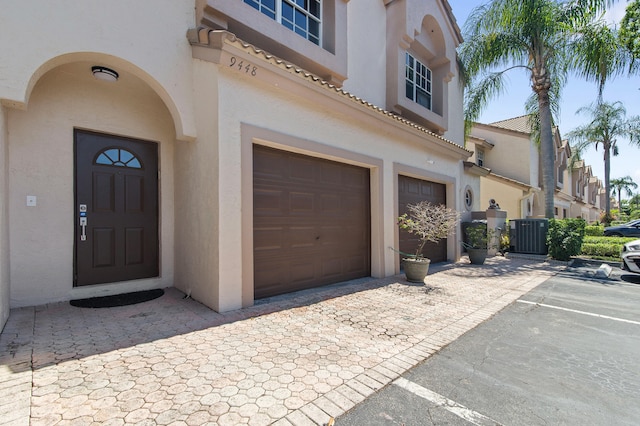 9448 Boca River Cir, Boca Raton, FL 33434 - doorway to property with cooling unit, stucco siding, an attached garage, a tiled roof, and driveway
