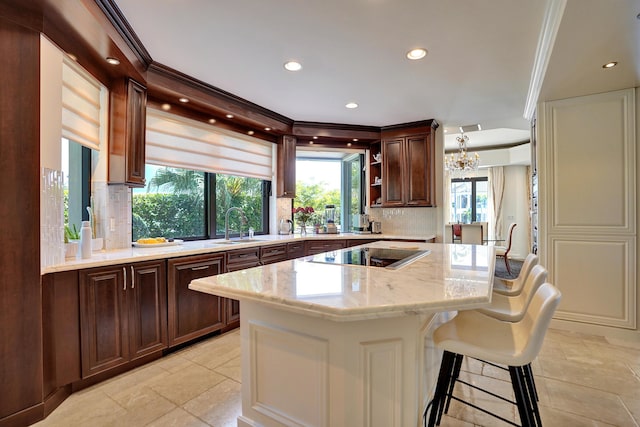 kitchen featuring black electric stovetop, a chandelier, a center island, backsplash, and light stone countertops