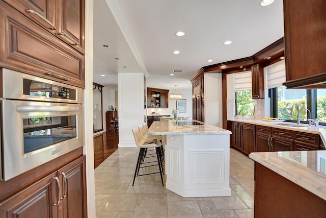 kitchen featuring a sink, a breakfast bar, recessed lighting, stainless steel oven, and light stone counters