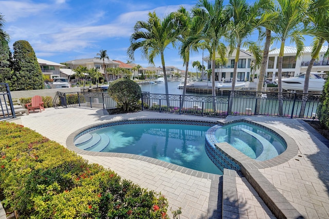 view of swimming pool featuring a residential view, a pool with connected hot tub, fence, and a water view