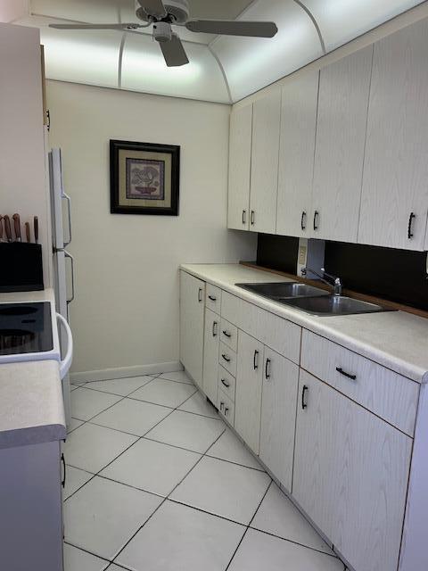 kitchen with light tile patterned flooring, light countertops, a sink, a ceiling fan, and baseboards