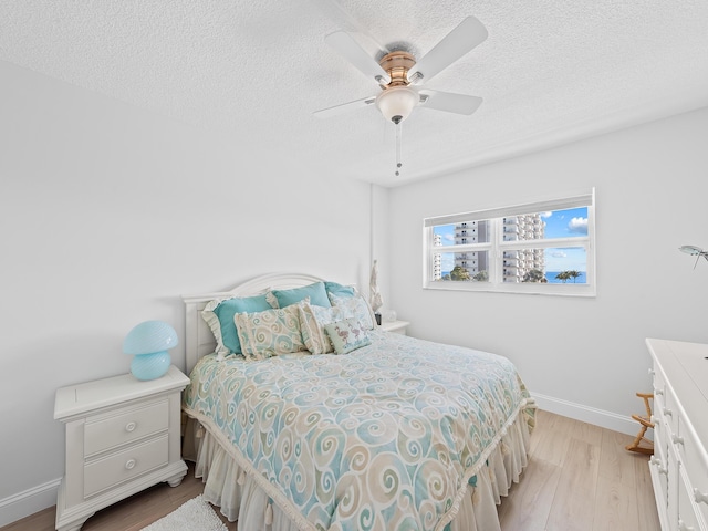 bedroom featuring ceiling fan, baseboards, a textured ceiling, and light wood-style flooring