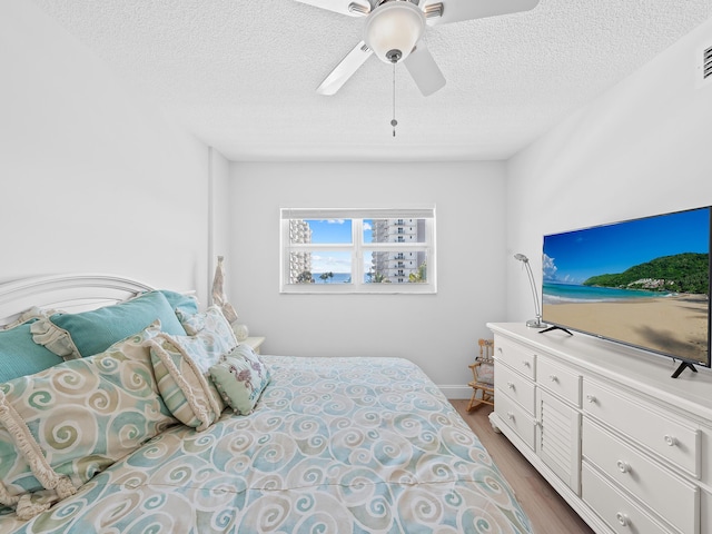 bedroom with a ceiling fan, wood finished floors, and a textured ceiling
