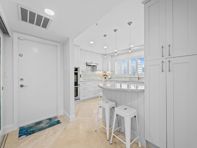 kitchen featuring light countertops, visible vents, decorative backsplash, a breakfast bar, and under cabinet range hood
